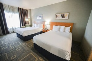 A hotel room with two beds, a nightstand, a lamp, and a window with curtains. - StripViewSuites at Platinum (Las Vegas)