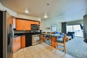 A modern kitchen with wooden cabinets, stainless steel appliances, and a dining area with a large window. - StripViewSuites at Platinum (Las Vegas)