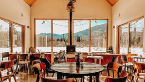 En restaurang med ett högt tak av trä, stora fönster med utsikt över bergen samt flera bord och stolar.