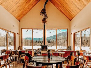 A restaurant with a high wooden ceiling, large windows with mountain views, and multiple tables and chairs. - Farouche Tremblant (Lac-Supérieur)