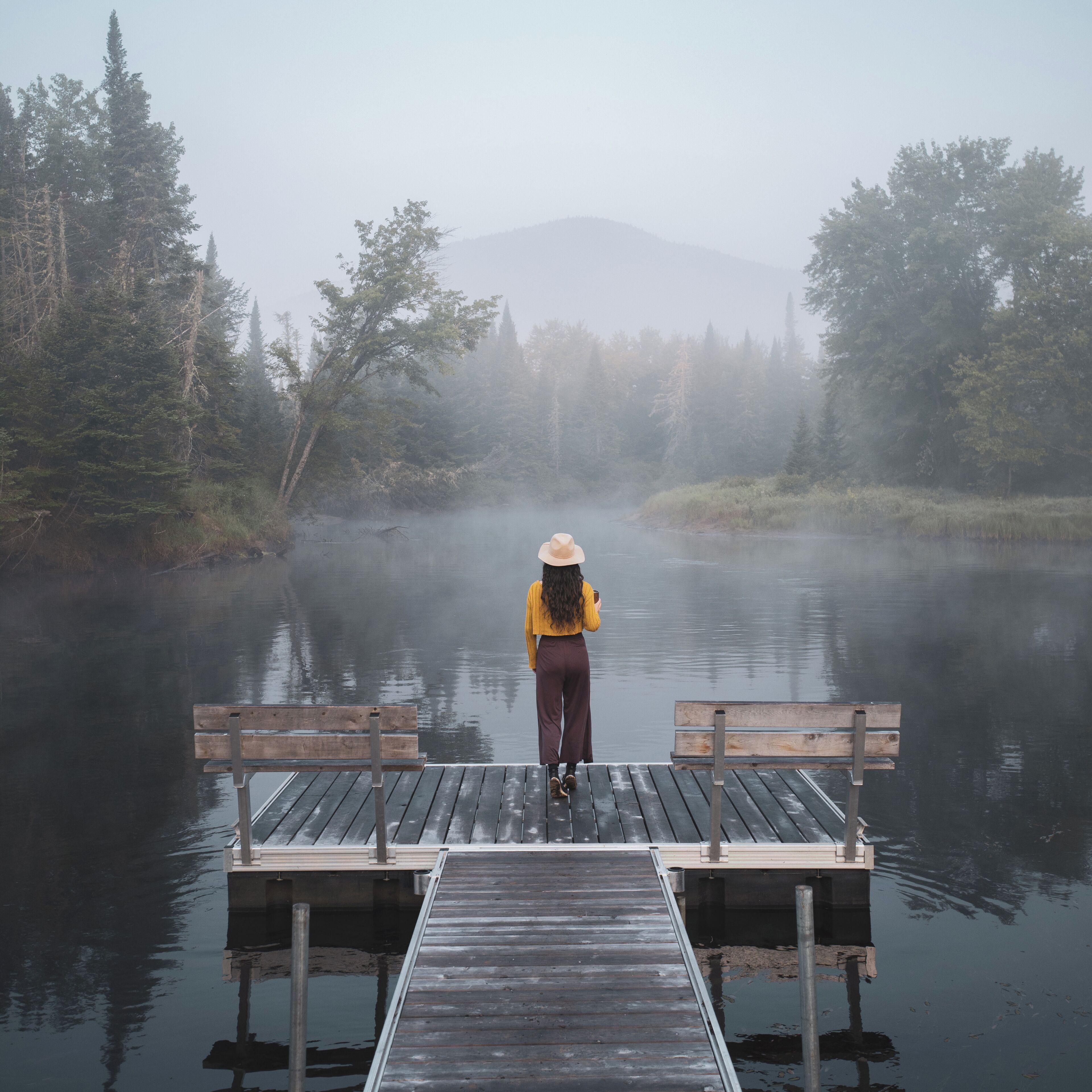 A wooden dock extending into a misty lake with dense forest on either side.