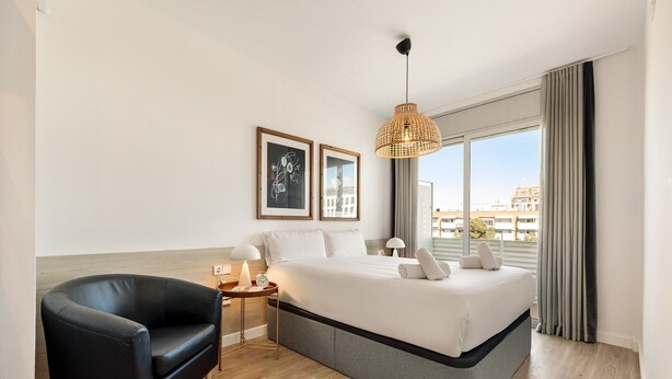 Una camera d'albergo moderna con un letto grande, una poltrona in pelle nera, un comodino con una lampada e opere d'arte incorniciate appese al muro.