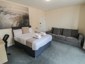 A hotel room with a bed, a grey sofa, a desk, and a painting on the wall.