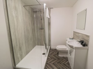 A modern bathroom with a glass-enclosed shower, a white toilet, and a sink with a marble countertop.