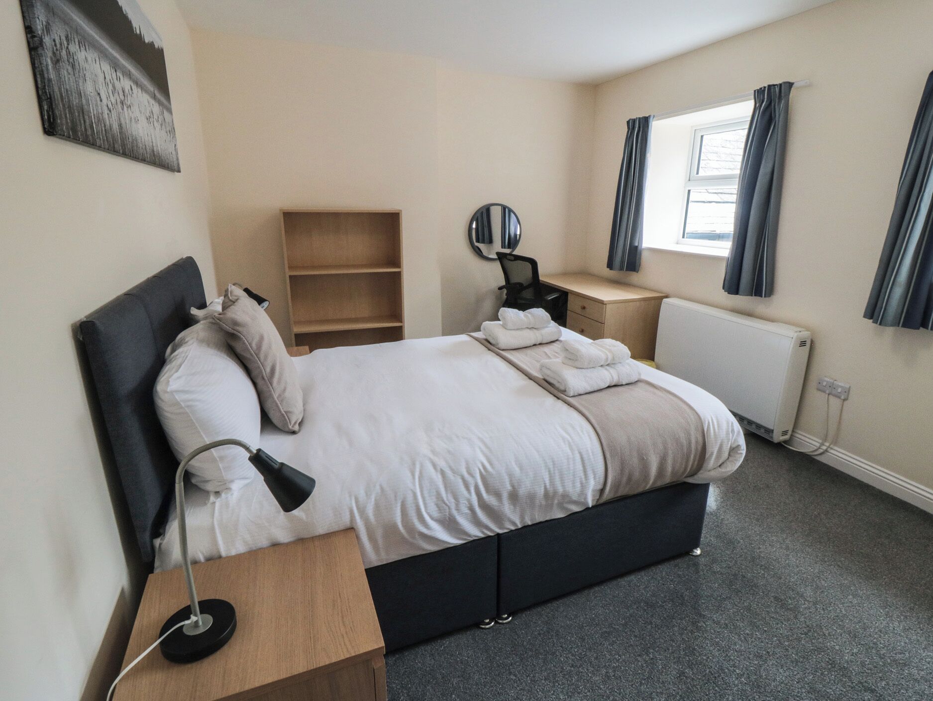 A neatly arranged bedroom with a bed, bedside table, desk, chair, and a radiator.