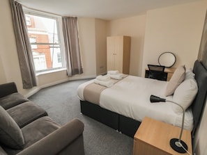 A hotel room with a bed, a desk, a chair, a wardrobe, and a window.