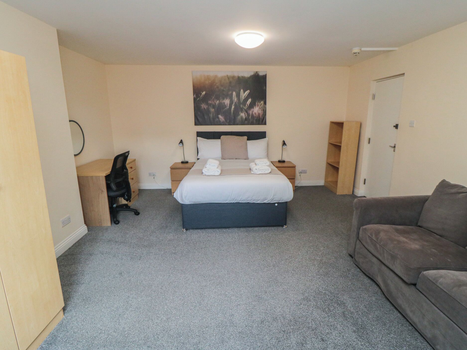 A hotel room with a bed, a desk, a chair, a couch, and a painting on the wall.