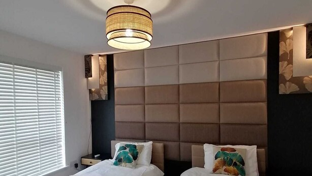 Une chambre moderne avec deux lits, une grande fenêtre équipée de stores et un revêtement mural au design original.