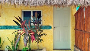 A yellow building with a thatched roof, a white door, and a wooden fence. - Hotel Maya Dreams (Bacalar)