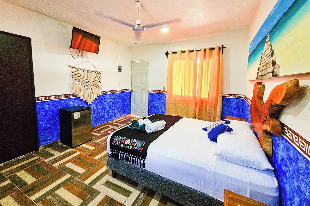 A hotel room with a bed, a ceiling fan, a television, a door, and a window with curtains.