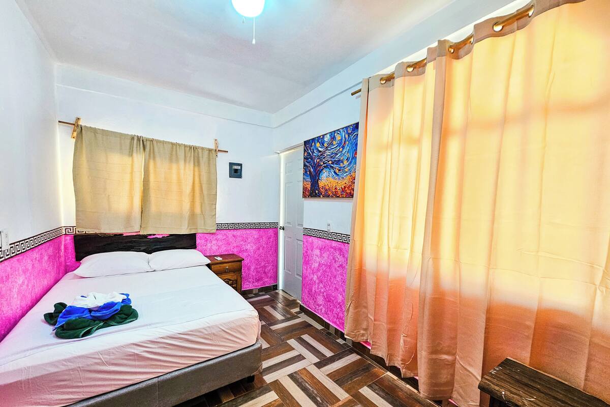 A bedroom with a bed, a nightstand, a wall-mounted painting, and a patterned floor.