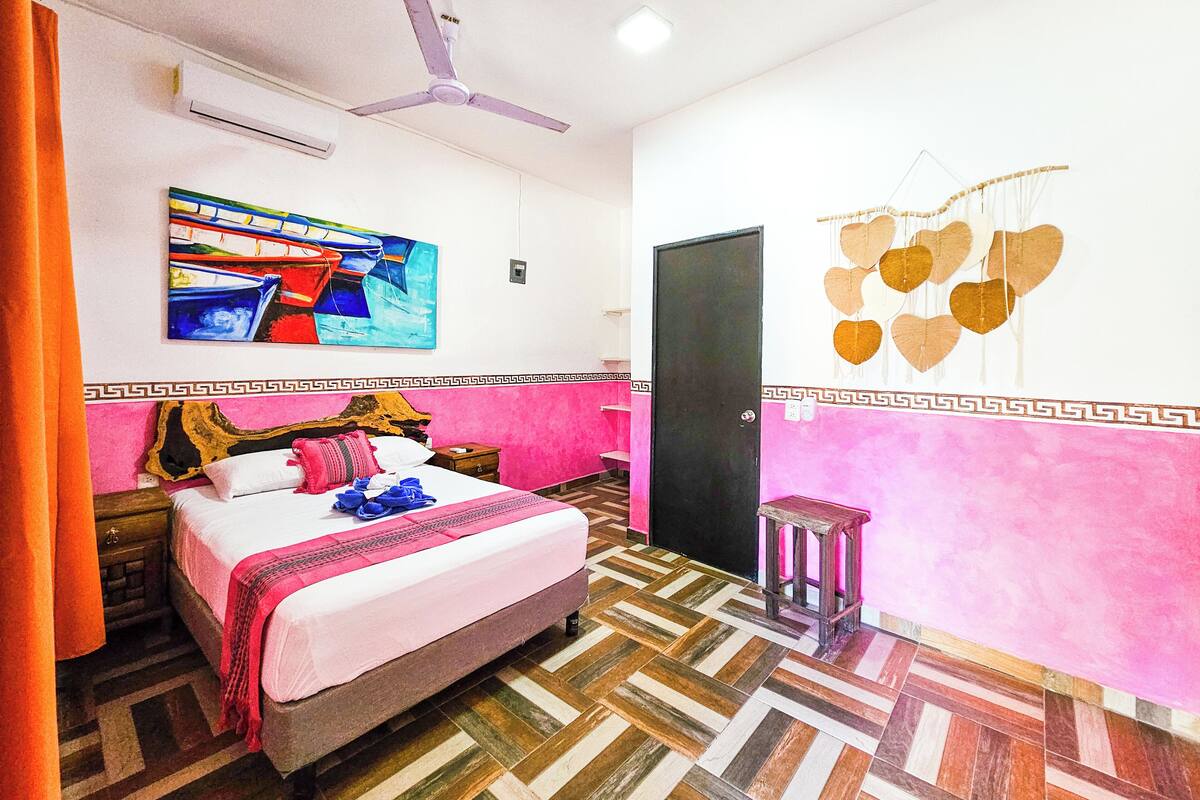 A bedroom with a bed, a ceiling fan, a painting, a door, and a wall decoration.