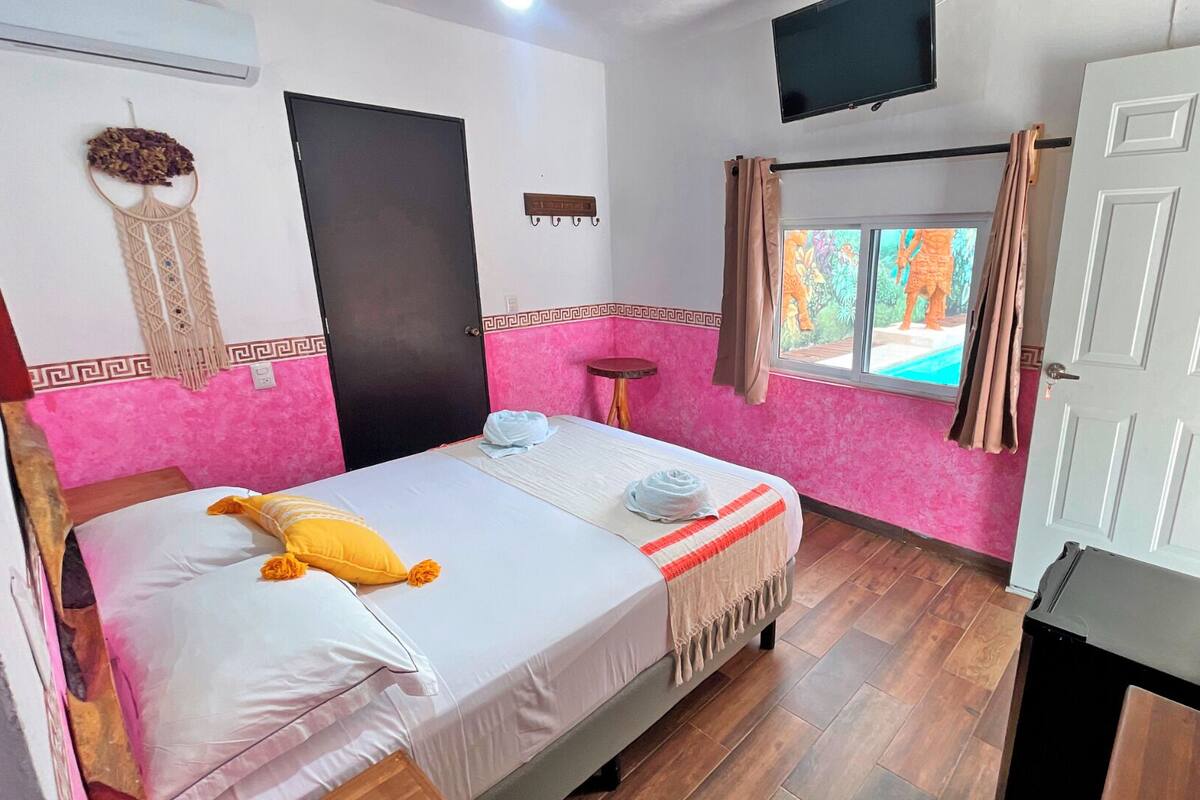 A hotel room with a bed, a TV, a window with curtains, and a door.