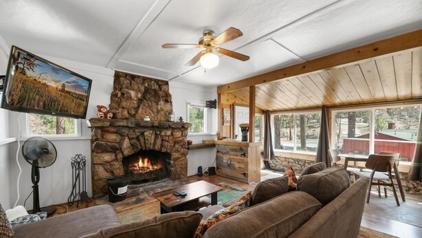 Una sala de estar acogedora con chimenea de piedra, ventilador de techo, televisor grande y una zona de estar confortable.