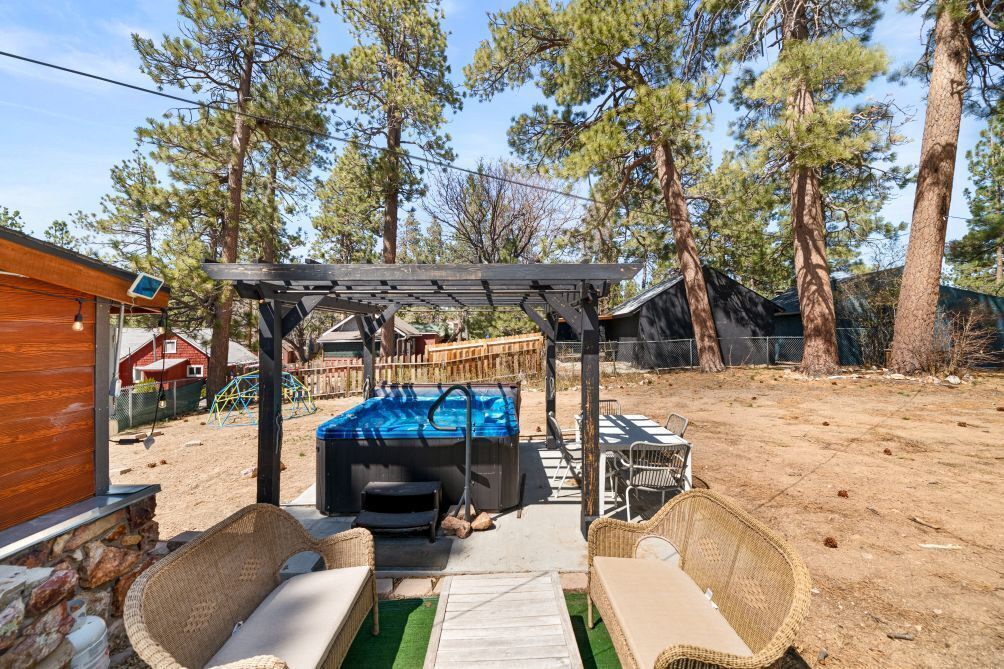 A backyard with a hot tub, outdoor furniture, and a pergola.