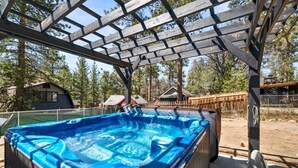 Un jacuzzi bajo una pérgola de madera con vista a cabañas y árboles.