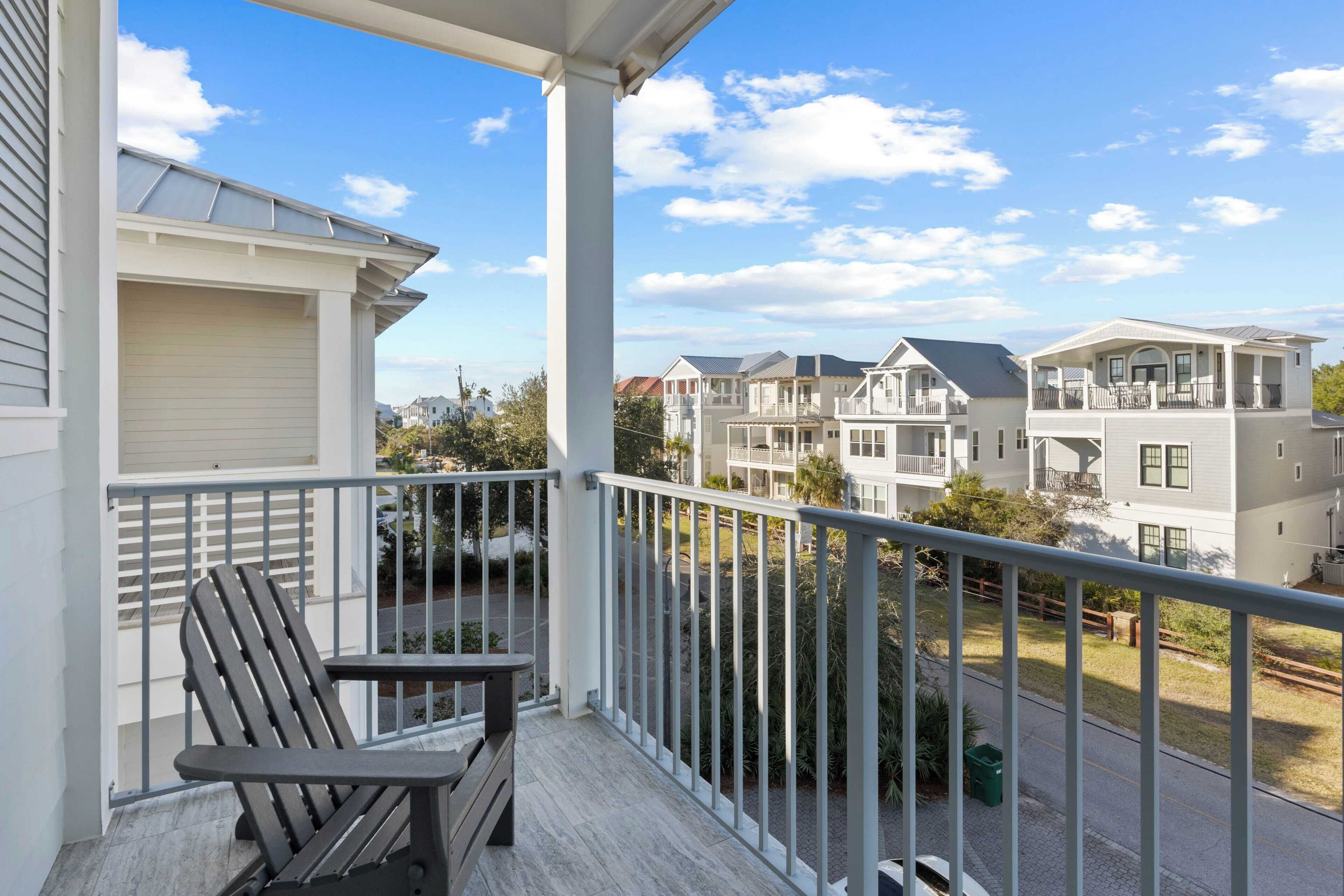 A balcony with a chair and a table, overlooking a residential area with multiple houses.