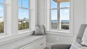 Una stanza con una panca integrata, ampie finestre e vista su un balcone e il mare.