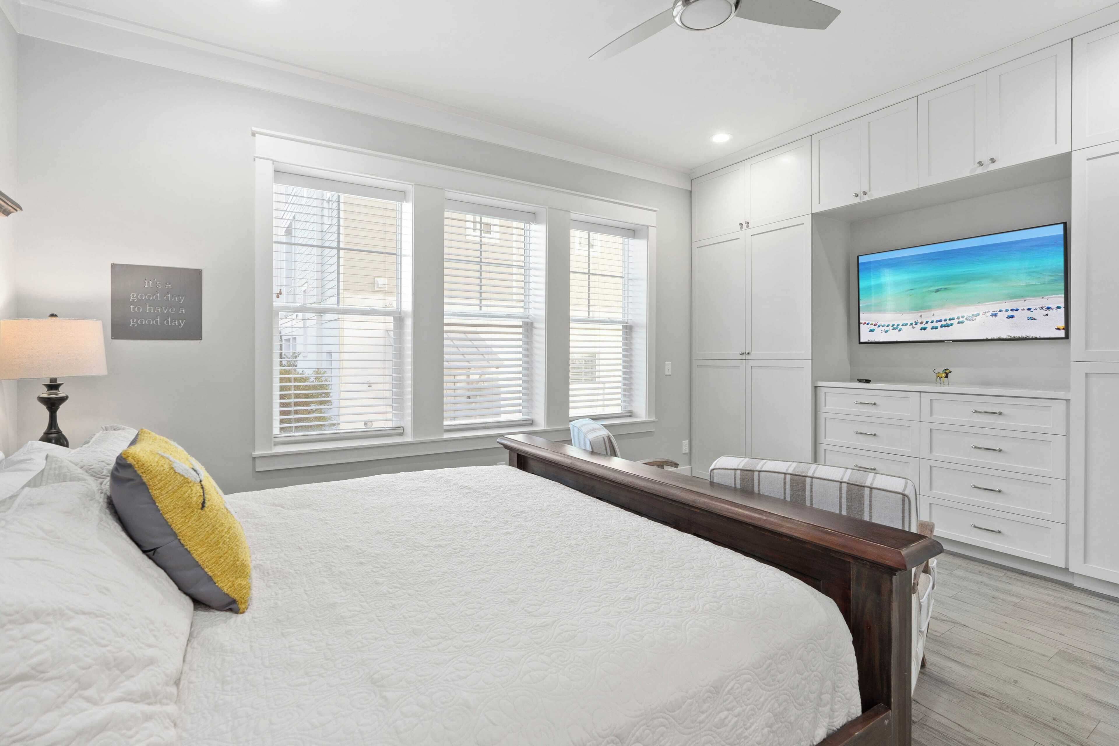 A bedroom with a large bed, a TV, and a window with blinds.