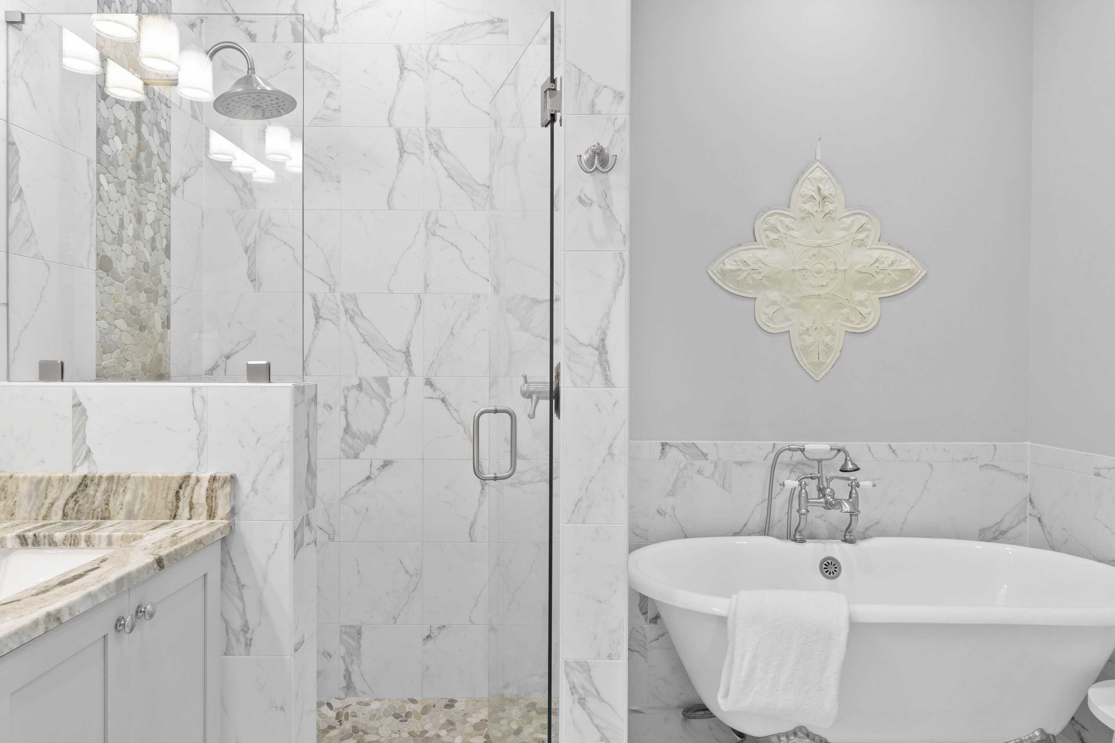 A modern bathroom with a glass-enclosed shower, a freestanding bathtub, and a marble-tiled vanity.