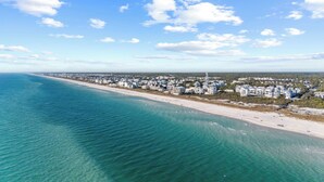 Una vista aerea di una cittadina costiera con una lunga spiaggia, acque blu cristalline e edifici bianchi.