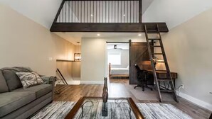Un espacio habitable tipo loft con una escalera de madera, un sofá, una mesa de centro y un escritorio.