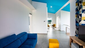 Ein modernes Wohnzimmer mit einem blauen Sofa, einem gelben Hocker und einem TV-Schrank.