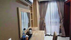 Habitación de hotel con un escritorio de madera, un espejo grande, cafetera, botella de agua y armario con espejo.