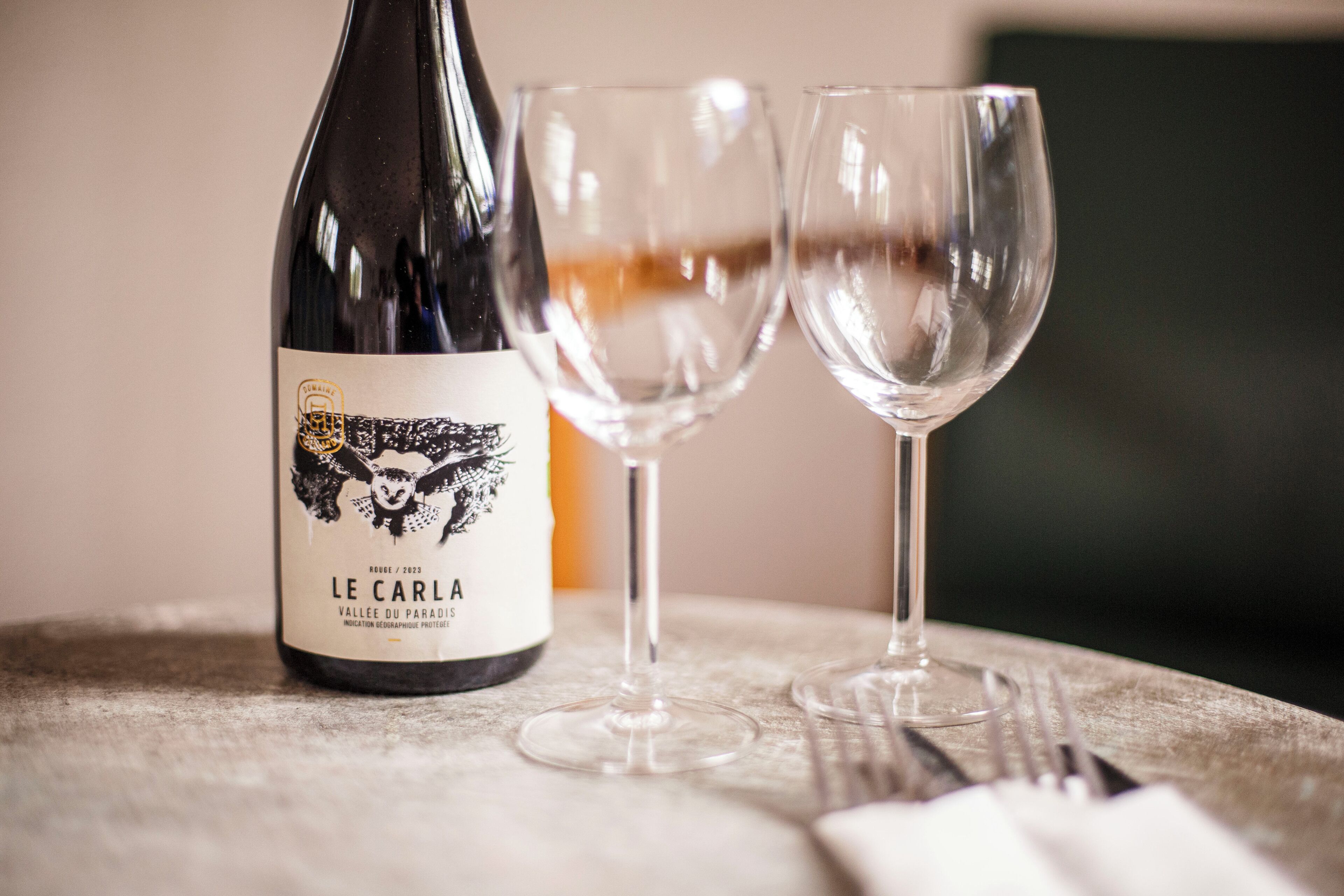 A bottle of wine with a label and two empty wine glasses on a table.