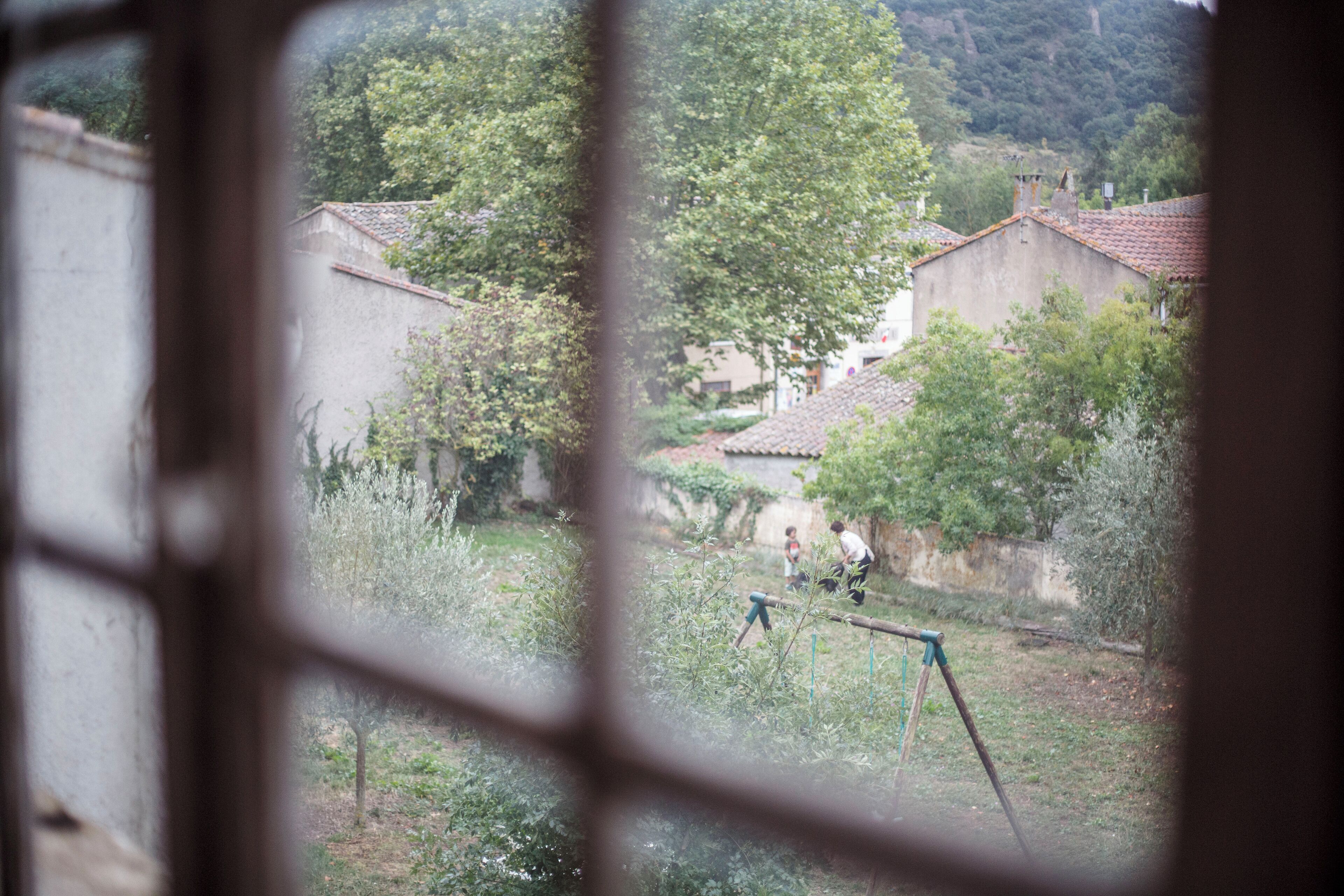 Paesaggio rurale visibile attraverso una finestra, con case, alberi e un’altalena.
