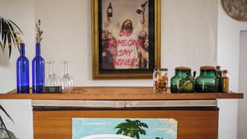 A wooden counter with blue and green glass bottles, clear wine glasses, and a framed poster on the wall.