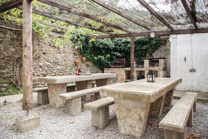 An outdoor patio with stone tables and benches, a pergola, and a stone wall with greenery. - Domaine Castelnaut gîte et château (Laroque-de-Fa)