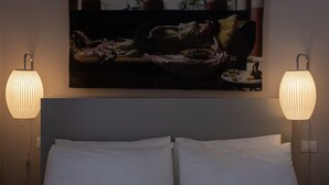 A hotel room with a bed, two wall-mounted lamps, and a painting above the bed.