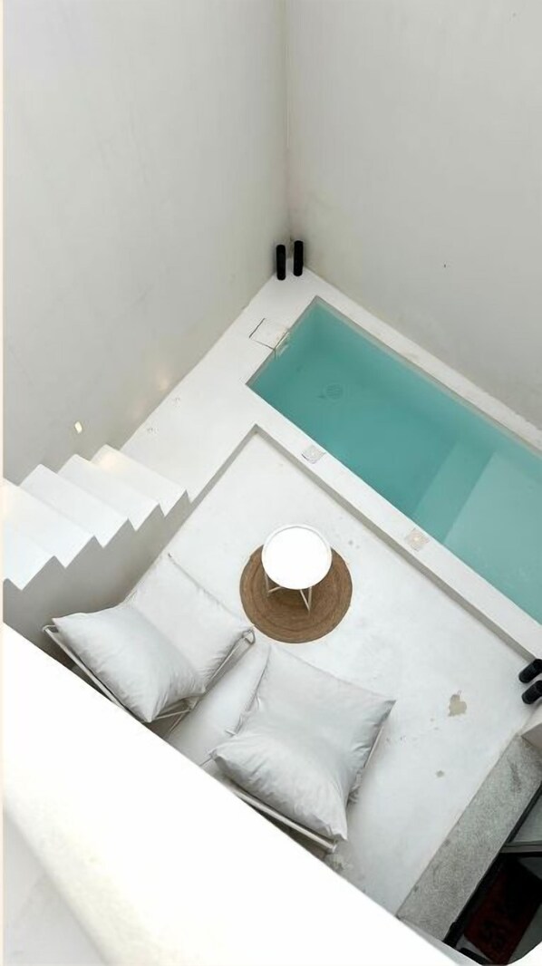 A modern bathroom with a bathtub, a small round table, and a bench with pillows.