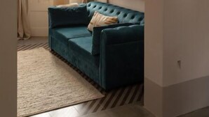 A living room with a teal sofa, a lamp, a tapestry, and a framed picture on the wall.
