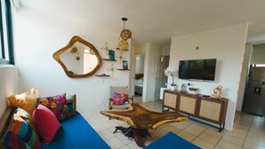 Una sala de estar con un sofá azul, una mesa de centro de madera, un televisor y objetos decorativos en estanterías.