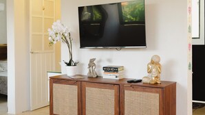 Una sala de estar con un televisor montado en la pared, un mueble de madera con objetos decorativos y una puerta blanca.