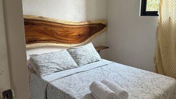 Une chambre à coucher avec une tête de lit en bois, une literie à motifs et une serviette enroulée posée sur le lit.