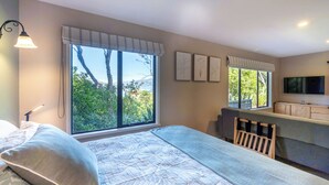 Une chambre à coucher avec un grand lit, un bureau avec une chaise, une télévision et de grandes fenêtres avec des rideaux.