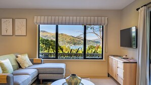 Un salon comprenant un canapé, une table basse, un meuble et un téléviseur. Une grande fenêtre offre une vue sur un paysage.
