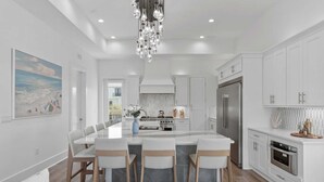 A modern kitchen with white cabinetry, a central island with bar stools, a stainless steel refrigerator, and a pendant light fixture.
