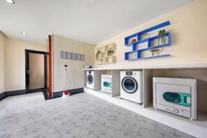 A laundry room with washing machines, a vacuum cleaner, and shelves with plants. - Xinyue Business Hotel (Dongguan)