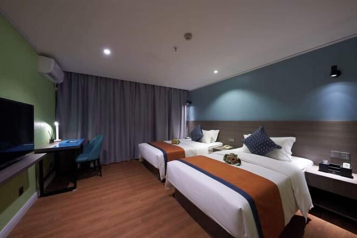 Habitación de hotel con dos camas, un escritorio, una silla y un televisor.