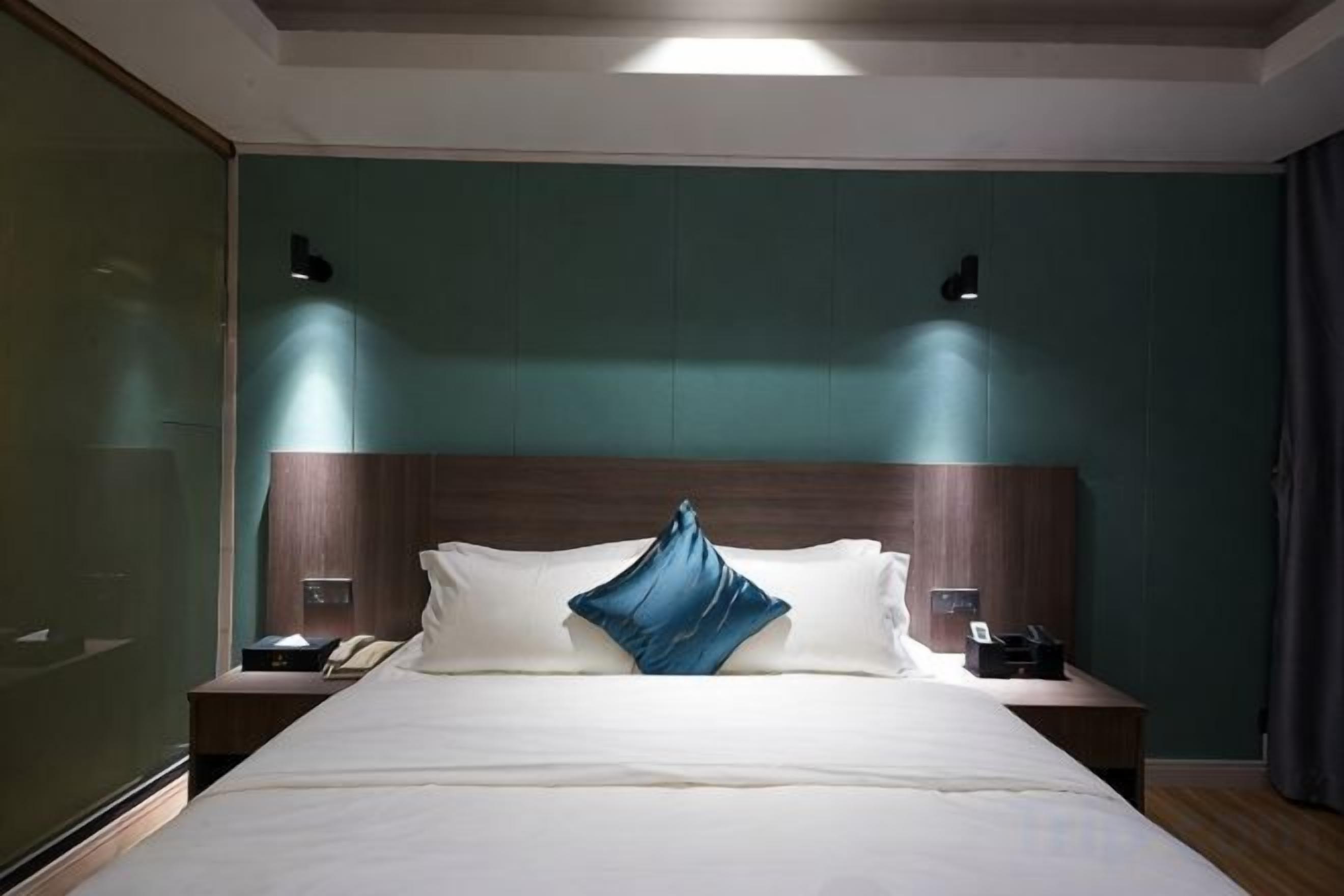 A hotel room with a large bed, two bedside tables, a nightstand, and a wall-mounted lamp.
