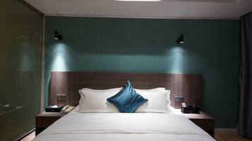 A hotel room with a large bed, two bedside tables, a nightstand, and a wall-mounted lamp.