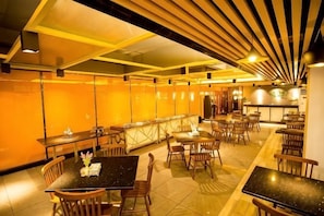 A restaurant with multiple tables and chairs, a bar area, and a high ceiling with wooden slats. - Xinyue Business Hotel (Dongguan)