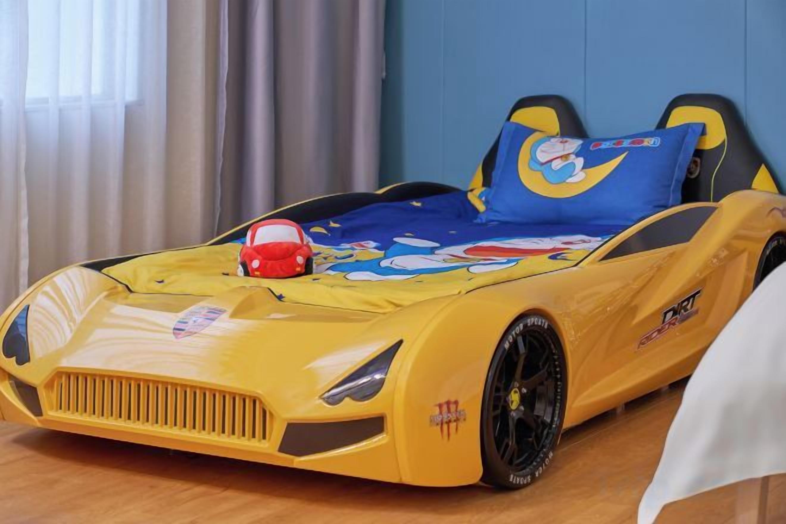 A child's bed with a cartoon car design, a pillow with a cartoon character, and a toy car.