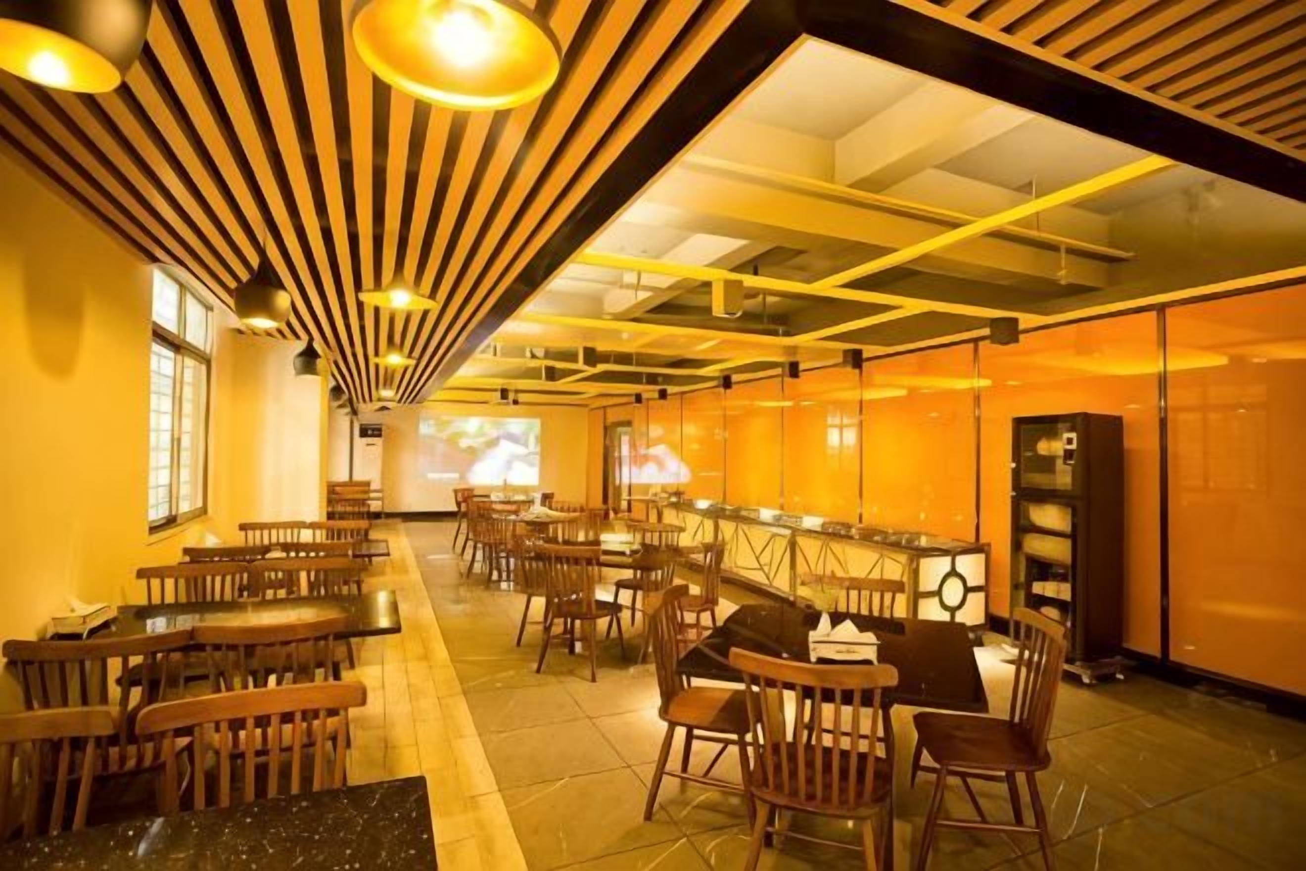 Een restaurant met verschillende tafels en stoelen, een bar en een projectiescherm aan de muur.