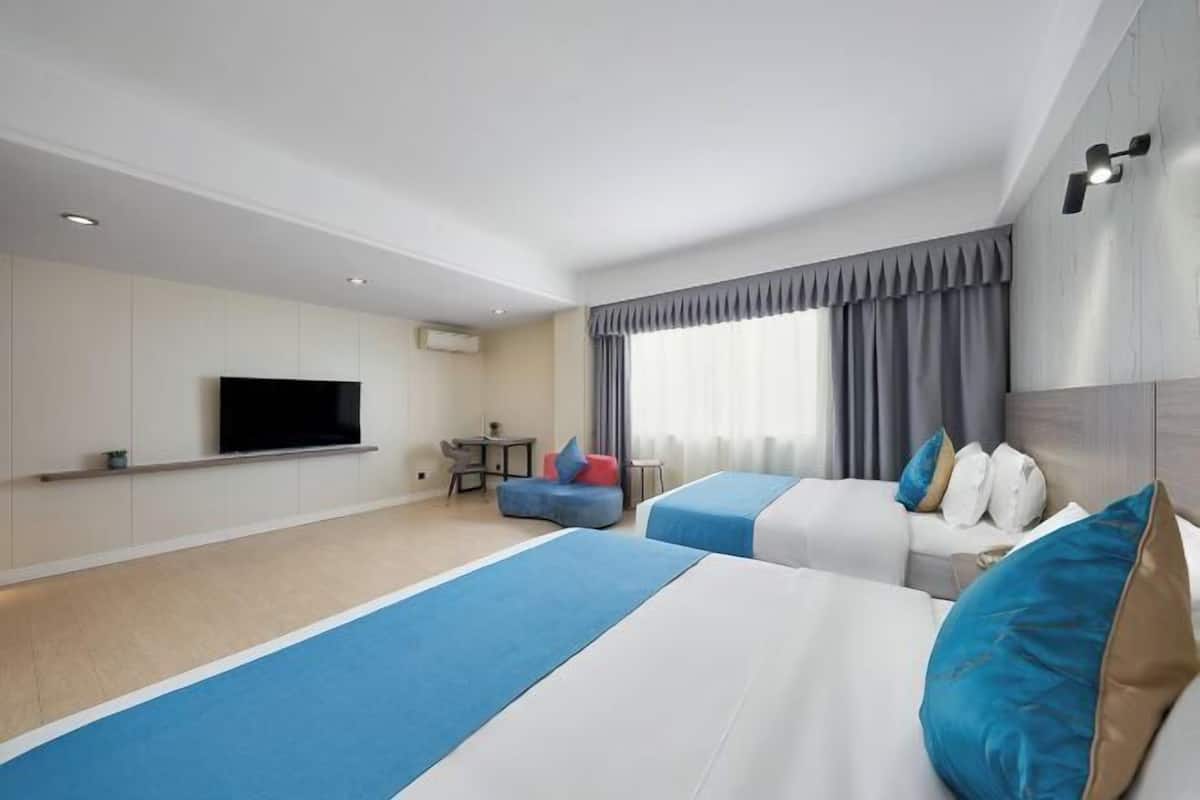 Habitación de hotel con dos camas, televisión, escritorio y ventana con cortinas.