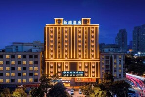 A multi-story hotel with illuminated signage, surrounded by urban buildings and a busy street. - Xinyue Business Hotel (Dongguan)
